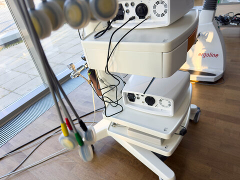 Klagenfurt, Austria - March 25, 2026: Medical rehabilitation equipment with multiple control panels and cables in a bright therapy room featuring large windows and wooden flooring