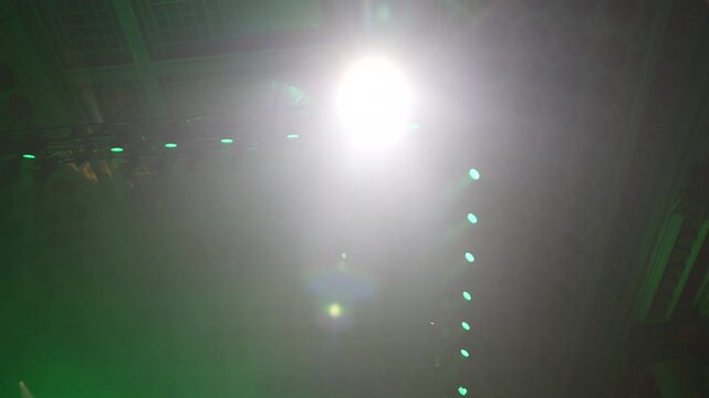 Bright green spotlights cut through the dark atmosphere of an empty stage or venue. The dynamic beams create circular patterns on the floor, evoking an energetic mood for a concert or live event.
