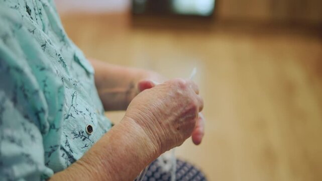 Elderly hands knitting yarn at home, closeup of grandmother crafting a soft scarf on her lap in warm sunlight, slow deliberate stitches, textured wool, calm nostalgic atmosphere suggesting heirloom