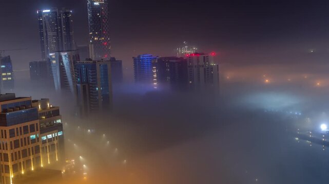 Spectacular night timelapse of blue neon buildings and street lights cutting through thick fog layer in Dubai Business Bay, with water canal reflecting glowing urban landscape.