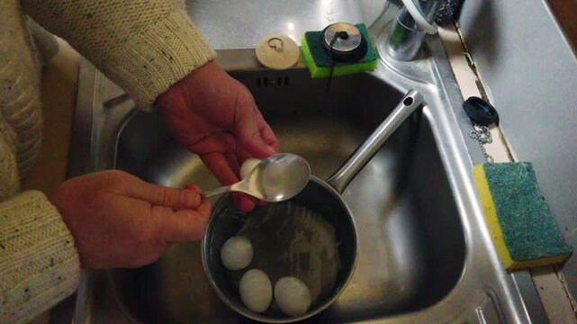 Detailed close-up of hands peeling hard boiled eggs directly in a pan. Perfect for cooking tutorials, breakfast prep videos, healthy meal content, and lifestyle clips.