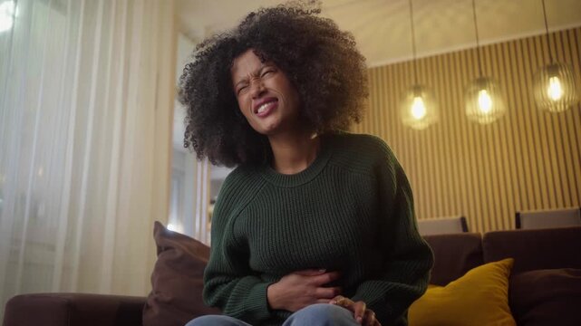 Stomach cramps, hands and woman on sofa in home with menstruation, periods or constipation. Tummy pain, sick and closeup of female person rubbing belly for IBS, endometriosis or virus in living room