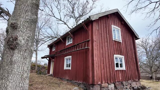 A historic wooden building in a public open-air museum in Sweden, captured in early spring 2026. The traditional structure is painted in classic falun red with white window frames and stands.
