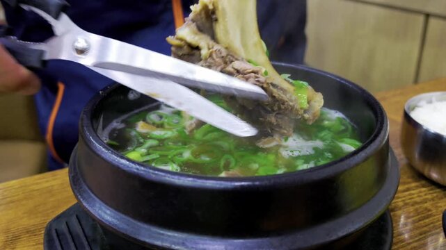 Galbitang or Korean Beef Short Rib Soup, man cuts meat with scissors