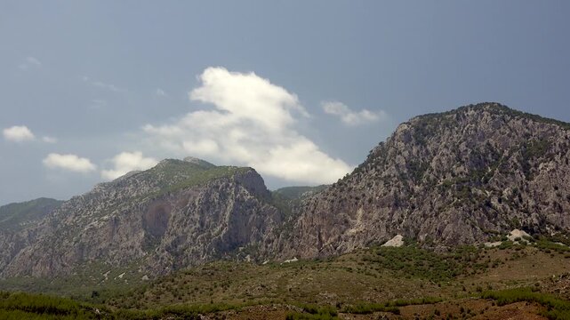 Timelapse clouds drift over Rocky Mountains forest landscape beneath clear blue sky. Fast motion cumulus forming across alpine ridgeline, wooded hillsides, bright daytime air.