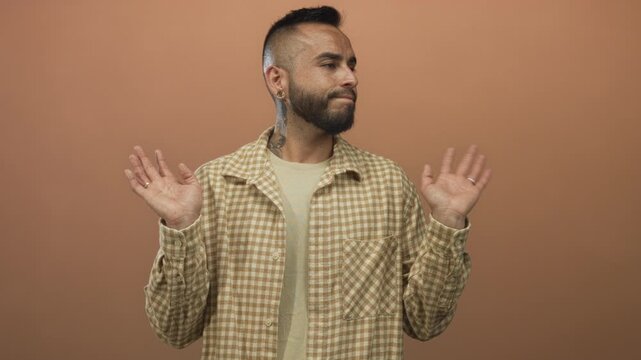 Man young hispanic with raised hands and closed eyes wearing checkered shirt in a terracotta studio backdrop; nonchalance.