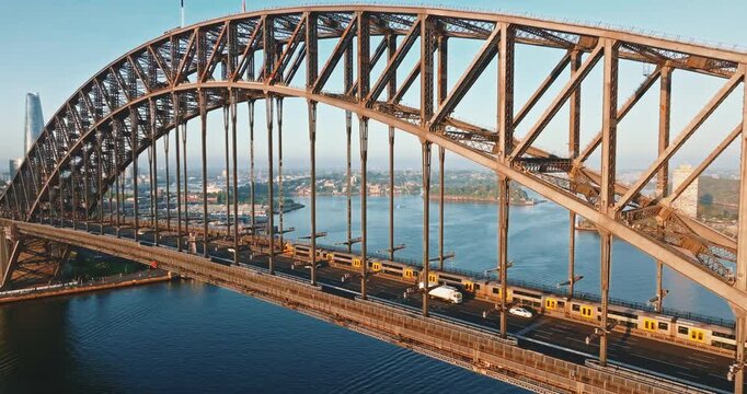 Sydney Harbour Bridge steel arch with cars and train riding across the water with city skyline and waterfront buildings in the background, modern cityscape view at daytime. Aerial drone static footage