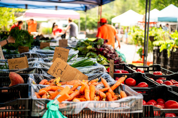 Obraz premium A colorful farmers market produce stand displays fresh carrots, leafy greens, and mixed vegetables with price signs, a vibrant scene of local food culture.