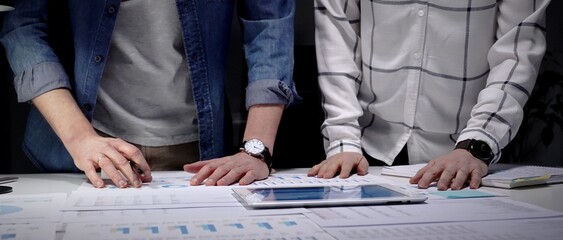 Business professionals analyzing financial data with charts and graphs on a tablet and paper, collaborating on market strategy and corporate growth planning in an office setting © volha_r