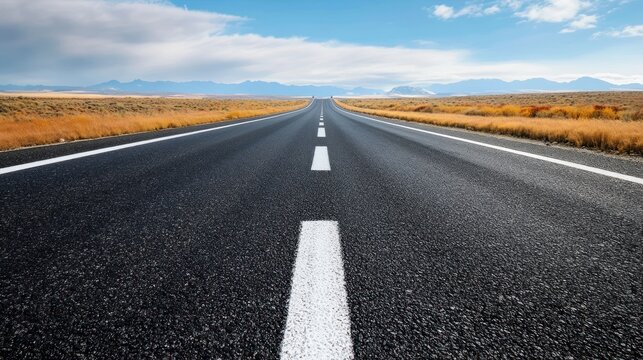 An empty highway stretches towards a mountain range under a blue sky