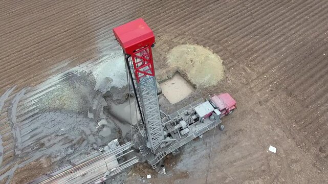 Water well drilling rig operating on farmland, aerial view of artesian well drilling process under clear sky. The machine penetrates deep into the ground for groundwater extraction and irrigation in a