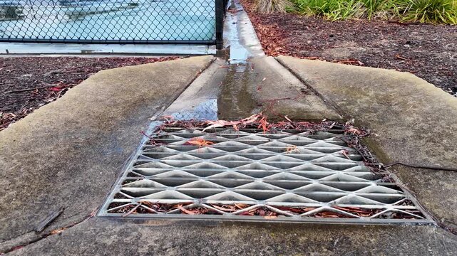 Stormwater flowing into grated drain from tennis court surface in suburban Melbourne Australia. Surface runoff channelled through designed concrete slope into urban drainage