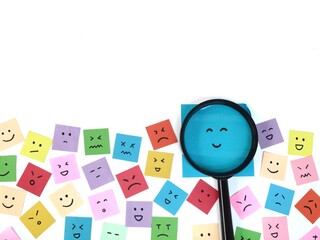 Fototapeta premium Magnifying glass over happy smiley face among various emotional expressions. Represents the complexity of mental health, mood swings, bipolar disorder diagnosis, and the search for happiness