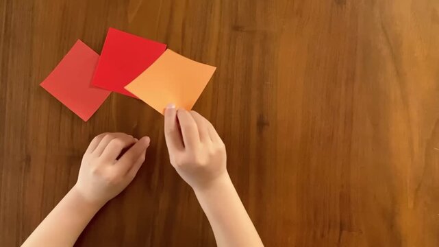 Placing the third colorful origami paper in sequence on wooden table, step by step arrangement, slow motion