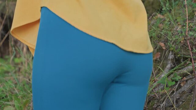 Closeup blue leggings on campsite yellow sweater hem waist and hip detail against green bush background textured fabric candid movement natural light lifestyle and apparel focus for stock use