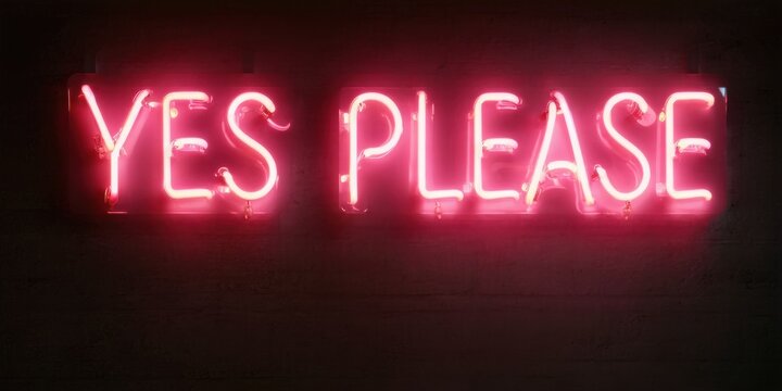 Bright pink neon sign displays words yes please against dark brick wall. Simple, bold lettering creates vibrant visual impact.