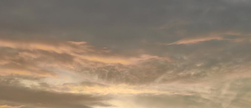   
  
Sunrise or sunset sky filled with clouds illuminated in warm orange pink yellow tones blending with grayish blue creating atmospheric gradient natural beauty scene