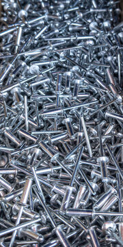 Pop rivets in chaos: a dense metallic scatter of fasteners with stems and rounded heads 