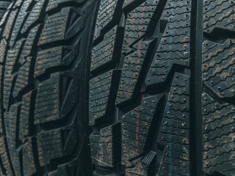 Macro detail of worn studded winter tire tread pattern with sipes, lugs, and stud holes visible