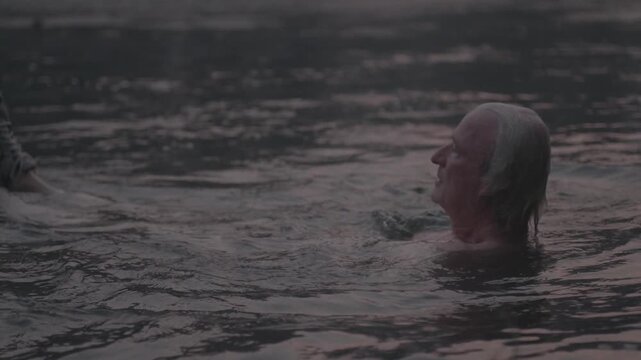 Desperate senior man struggling in the water, sinking and drowning under the surface at dusk