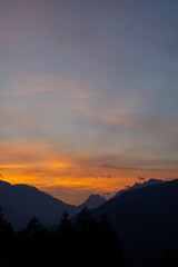 Obraz premium Spectacular sunset over a dark mountain range with silhouetted pine trees. Vibrant orange and yellow sky contrasting with dark alpine peaks. Mountain sunset background wallpaper 
