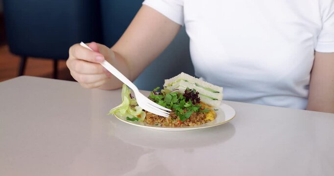 Passenger woman in white t shirt eating buffet meal of fried rice and sandwich with plastic fork, enjoying her quick lunch break at lounge in Chinese airport. Camera focused on plate with meal