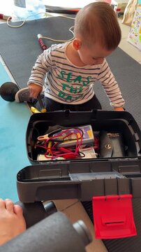Curious toddler exploring open toolbox with wires at home