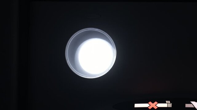 Close-up low angle shot of overhead passenger reading light in modern airplane economy class cabin. Ceiling lamp as it smoothly fades in, reaches full brightness, then gradually turn off