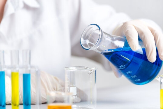 Scientist pouring blue liquid into empty beaker, laboratory experiment and chemical preparation for analysis