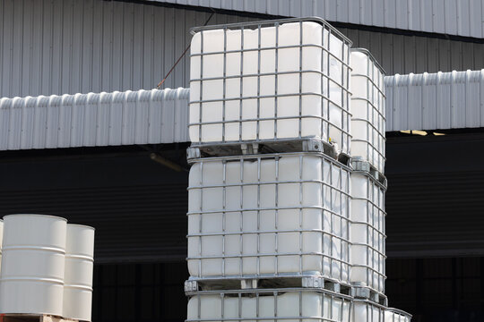 white ibc container in outdoor stock yard of factory, white plastic chemical tanks. The containers are piled on top of each other.