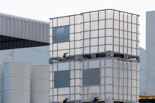 white ibc container in outdoor stock yard of factory, white plastic chemical tanks. The containers are piled on top of each other.