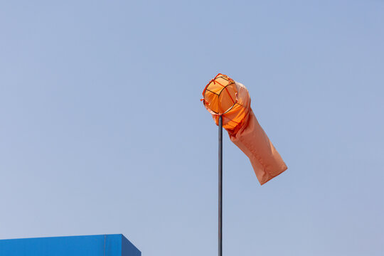 Orange wind sock against blue summer sky with factory background.