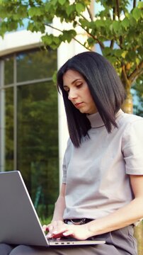 Focused young causian businesswoman using laptop pc online application for work sitting outdoors. People and Technology Concept.