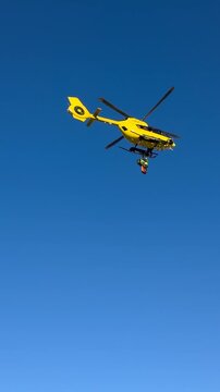A rescue helicopter in flight lowers doctors onto the ski slopes with a winch.