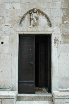 The gothic portal of the Church of Saint Nicholas in Korcula features a stone relief of Jesus the Good Shepherd in the pointed tympanum above a wooden door