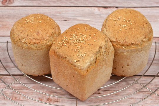 Three golden brown baked bread rolls topped with quinoa seeds resting on a metal cooling rack over a wooden surface