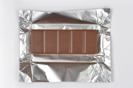 A rectangular milk chocolate bar lies centered on an open silver foil wrapper against a plain white background