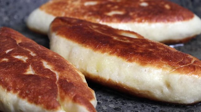 A close-up of potato pies being fried in a frying pan. The cook flips the pies with a fork.