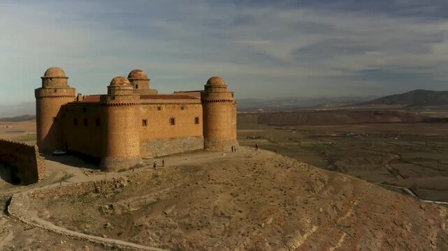 An ancient stone castle stands proudly on a desert hill