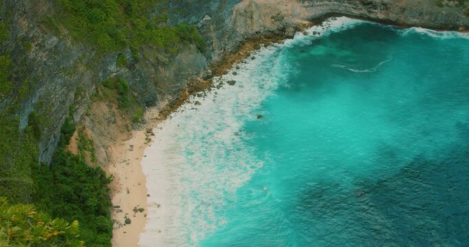Cliff framed view of foamy ocean waves along sandy beach in Nusa Penida Bali Indonesia