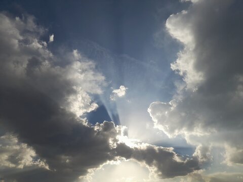 Sunbeams breaking through dramatic dark clouds in a deep blue sky, divine light effect, nature background