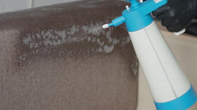 White Man Applying Foam To Sofa Armrest, Targeted Stain Treatment, Controlled Sprayer, Visible Bubbles Forming, Gloved Hand, Closeup Fabric Texture, Indoor Living Space, Precise Application For Lift
