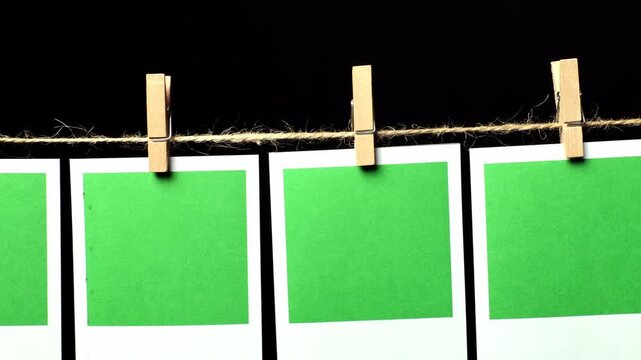 A row of green pieces of paper with a white frame against a black background. The camera pans from left to right, looking down the row of papers. Space for text.