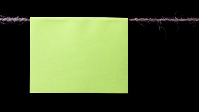 A square piece of yellow paper hangs on a thin rope against a black background. Space for text.
