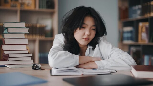 Tired asian student falling asleep at library desk