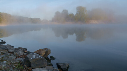 A tranquil morning scene of a lake with mist rising above the calm water and trees