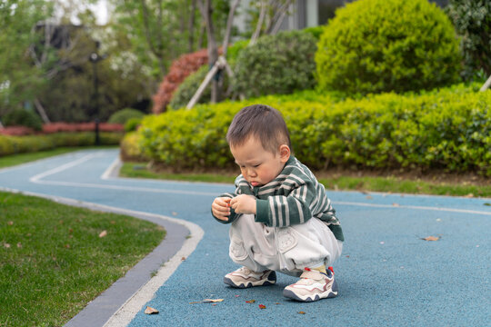 Medium shot of an Asian boy squatting on a race track, gazing intently at a leaf held carefully in his hands.