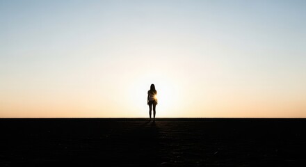 Fototapeta premium Lone figure silhouetted against a vibrant sunset, standing on a dark horizon.