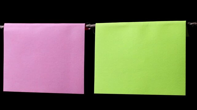 Two square pieces of pink and green paper hang on a thin rope against a black background. Space for text.