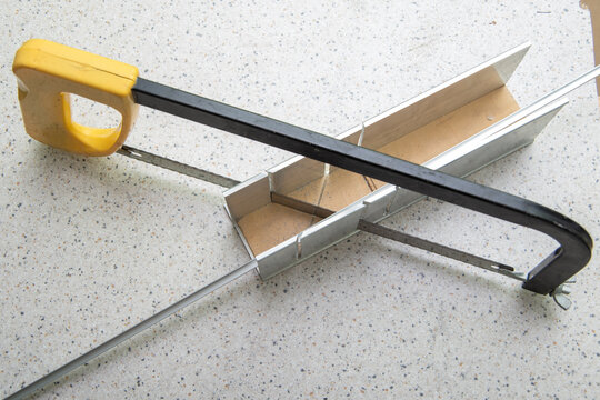 Hand saw with yellow handle positioned on a cutting guide for precise home furniture repair, showcasing metal and plastic materials on a work surface